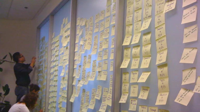 People grouping sticky notes into columns on a wall during an onboarding planning session.